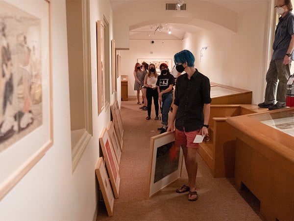 Students browse art selections in a museum hallway.