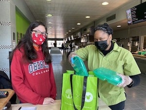 A masked student receiving their meal from a masked AVI staff member.