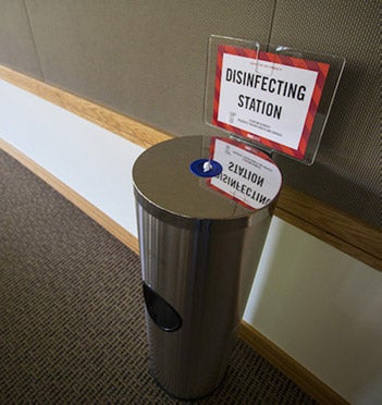 A dispenser of wipes in a corridor. Sign reads 'Disinfecting Station'.