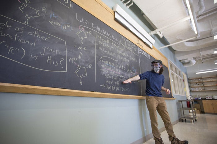 A professor in a COVID mask teaches at a blackboard.
