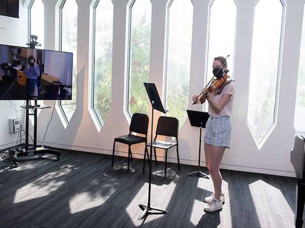 A violist plays in a Bibbins Hall classroom while the professor looks on from a remote video screen.