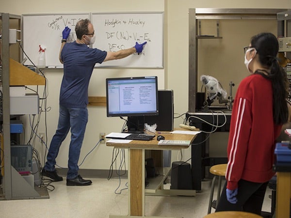 A professor points to equations on a whiteboard for his remote students.