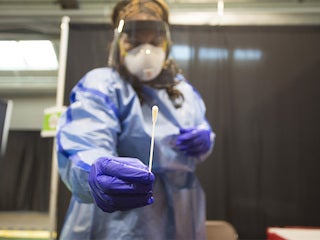 A health professional in PPE holds up a nasal swab.