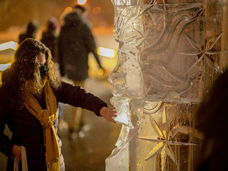 In winter clothes and a mask, a student examines the details of a large ice sculpture.