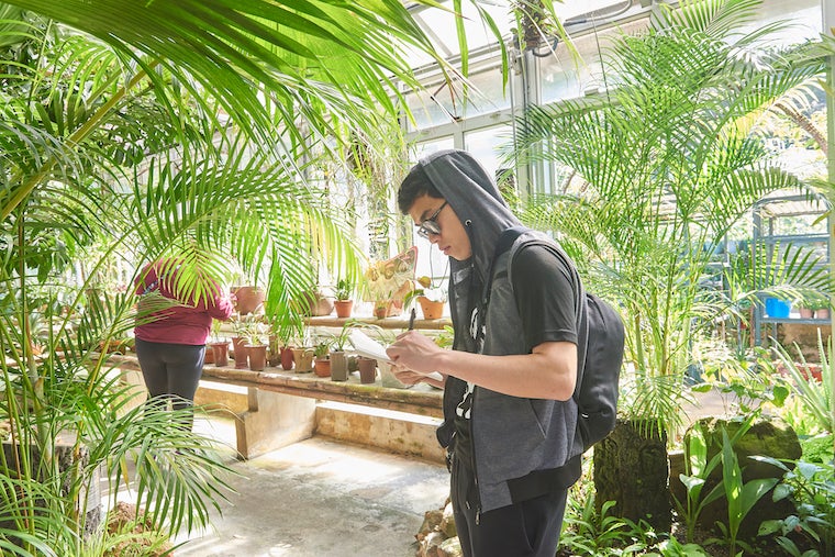 Image of student writing in notebook in greenhouse