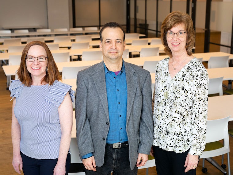 three people, woman, man, woman, standing in classroom