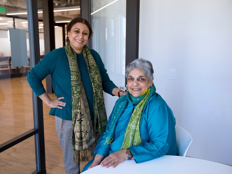 one woman stands with arm on the other woman who is sitting in a chair