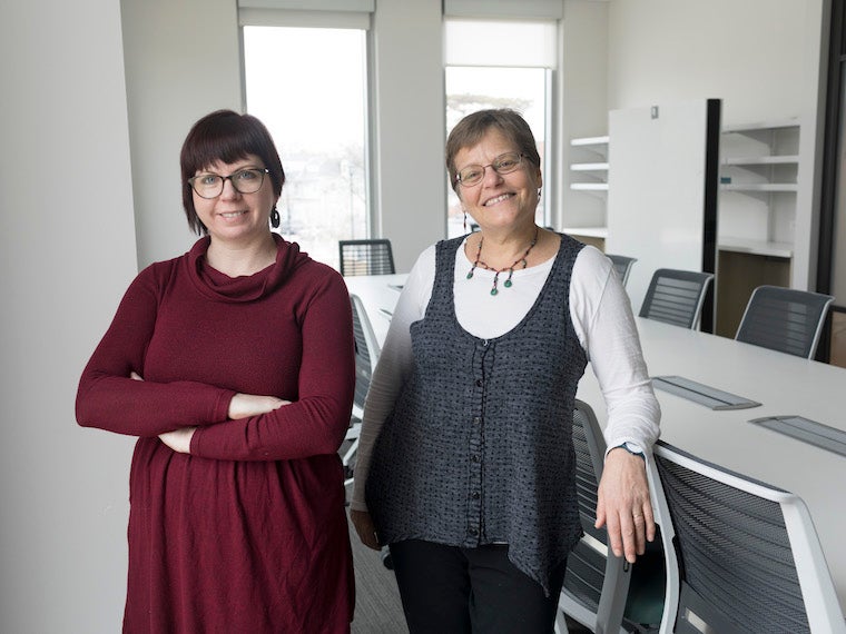 Two women standing next to a long white and gray table. Photo.