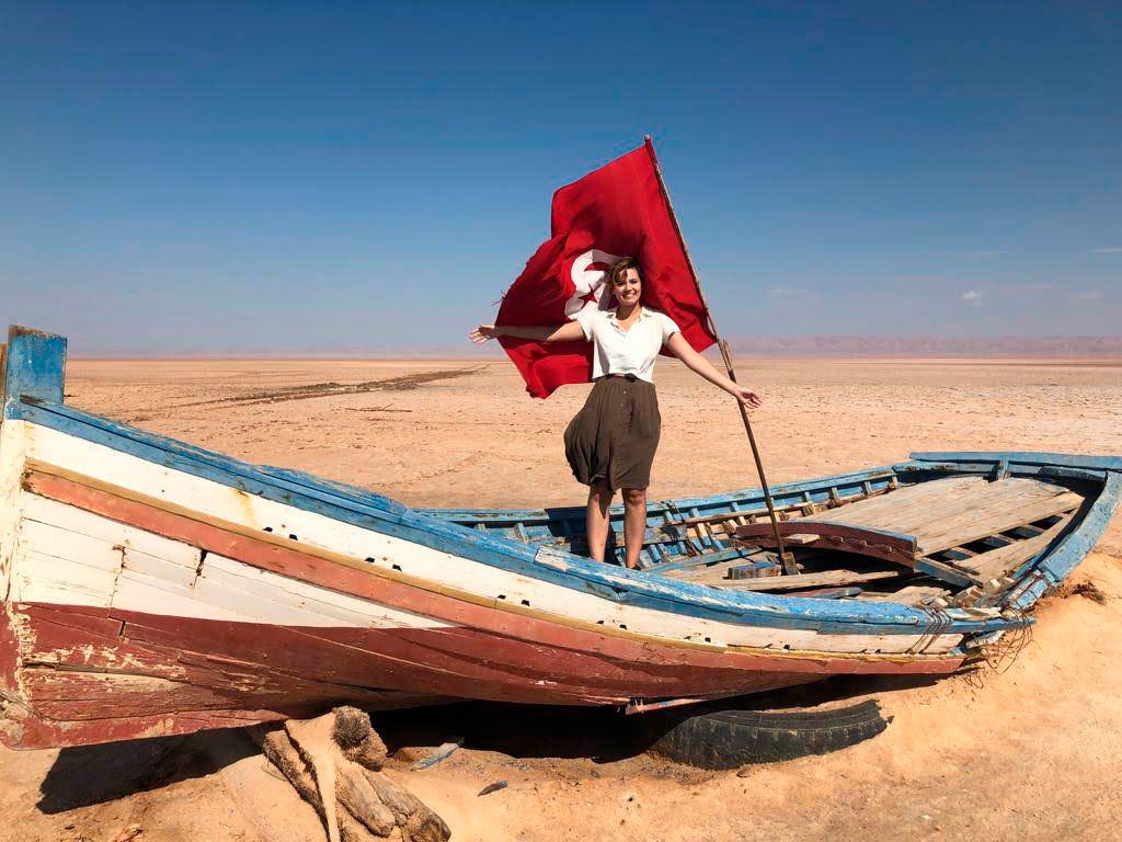 A student stands on the wreckage of a boat in the desert.