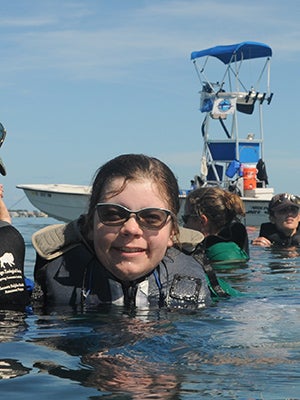 Larissa and her colleagues chest-deep in the ocean in front of a boat