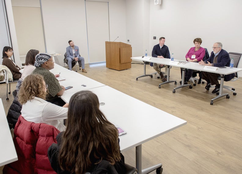 Students listen to three panelists in front of a room.