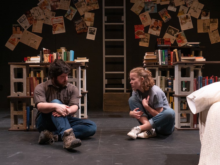 A girl and man sit on the floor in the middle of a room.
