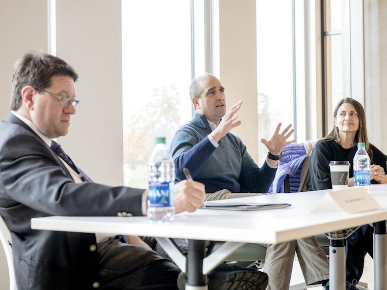 A panel of three professionals sit in front of a classroom.