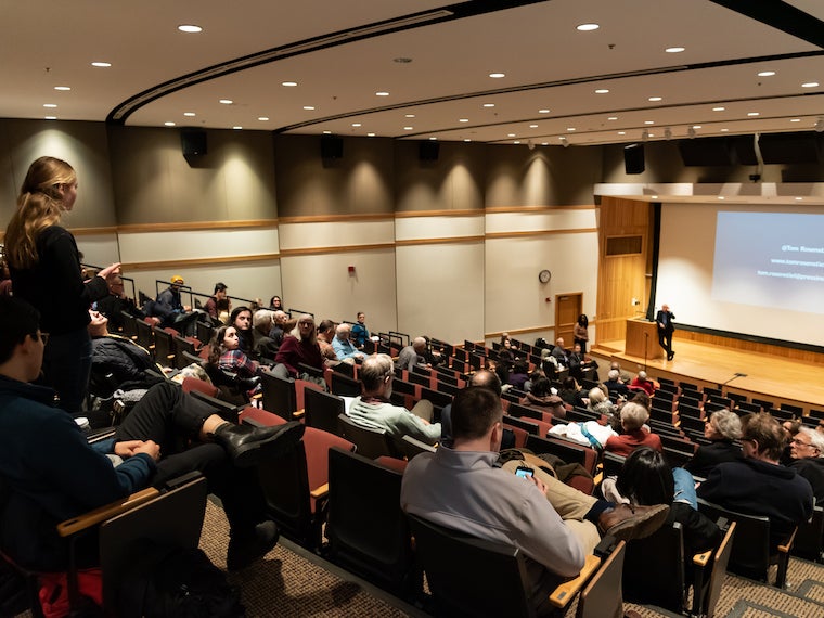 A girl stands and asks a question to a speaker on stage.