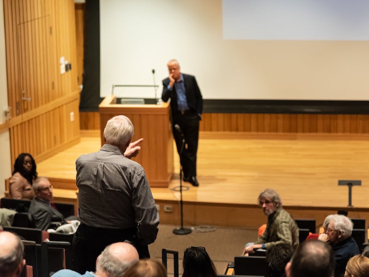 A man stands and points his finger at a speaker on stage.
