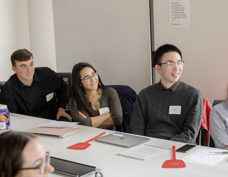 Three students in a conference room look toward the front of the room