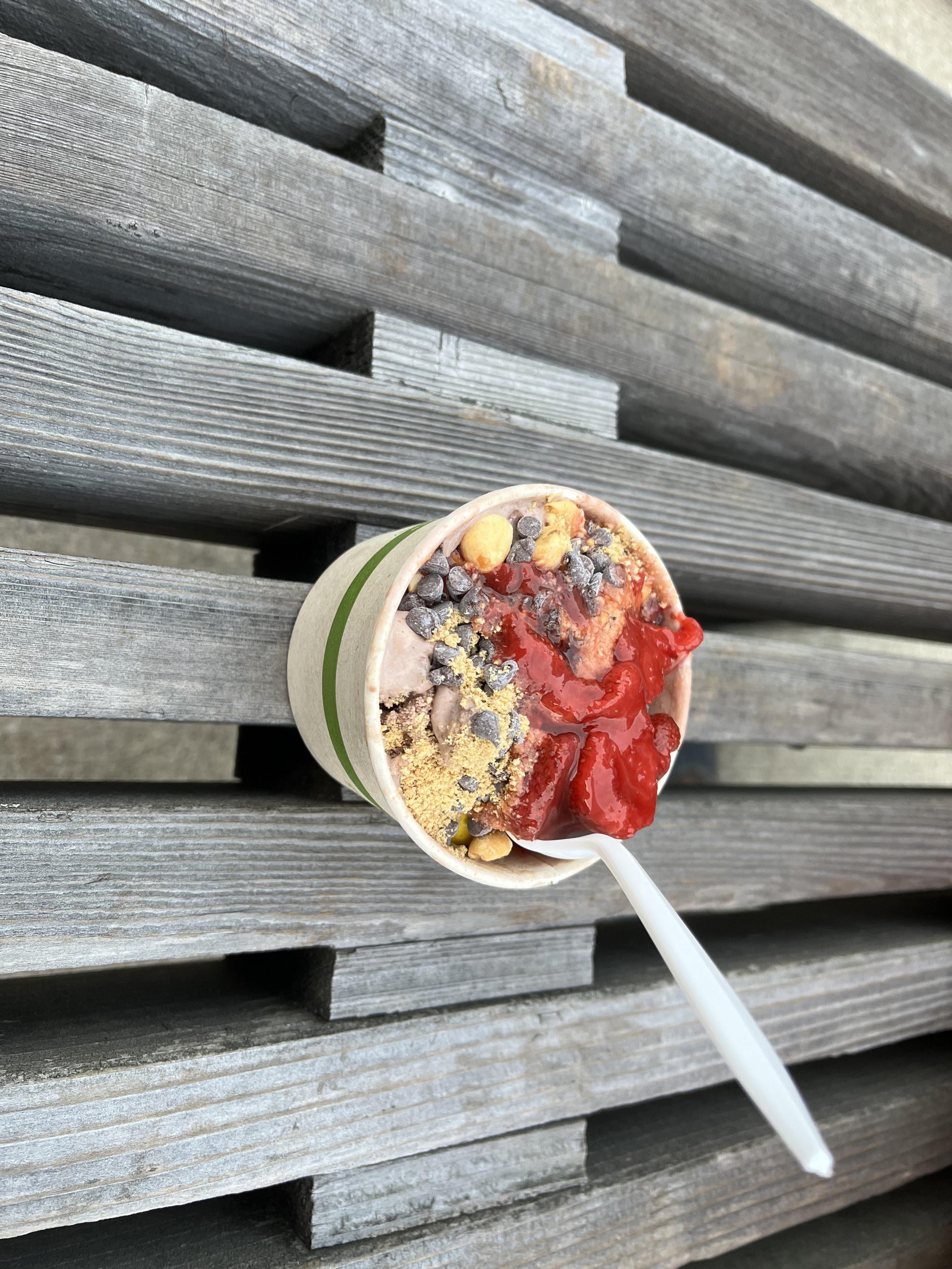 A tasty looking bowl of ice cream loaded with toppings on a wooden bench.