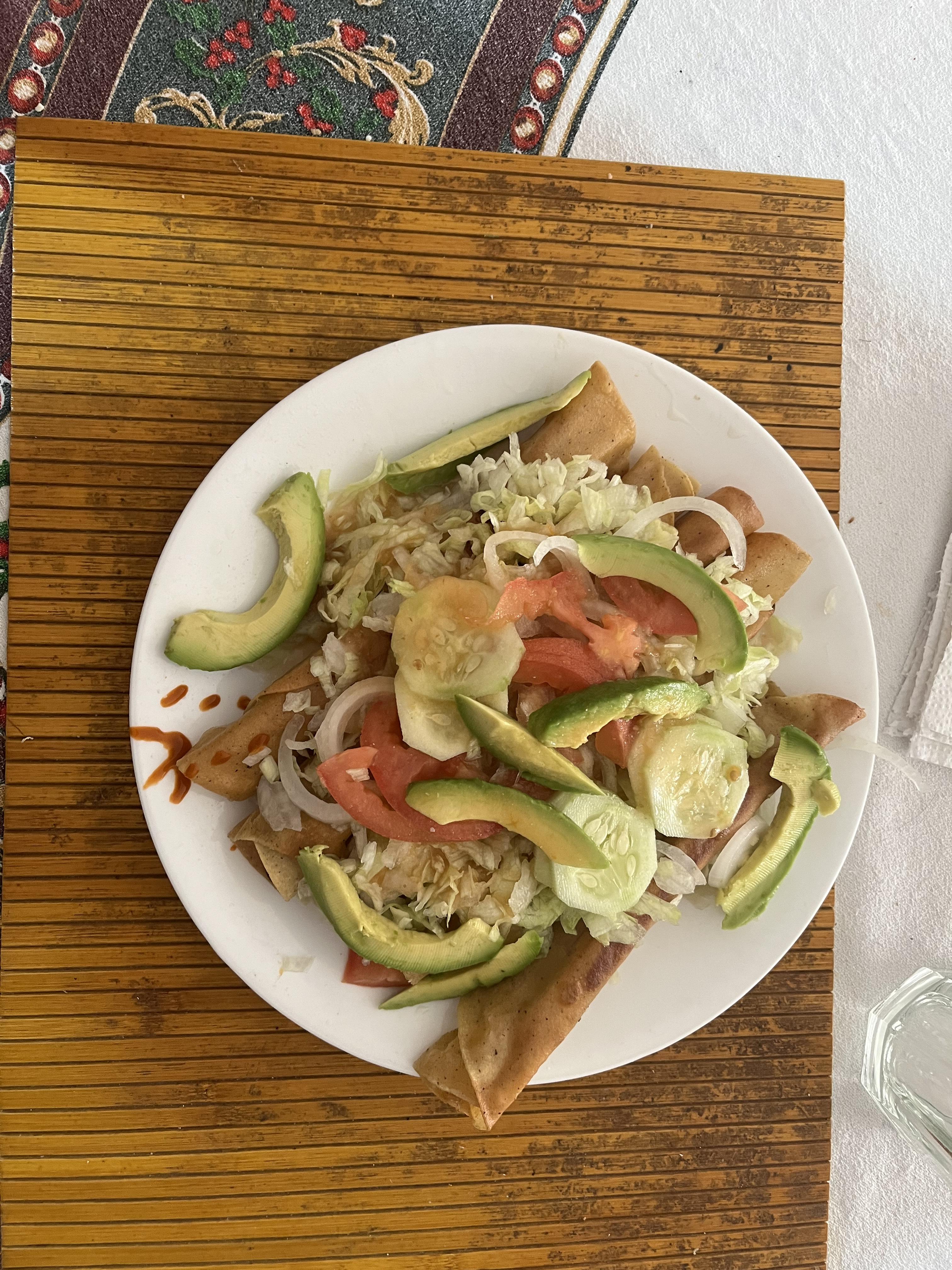 A meal of taquitos, vegetables, and avocado.