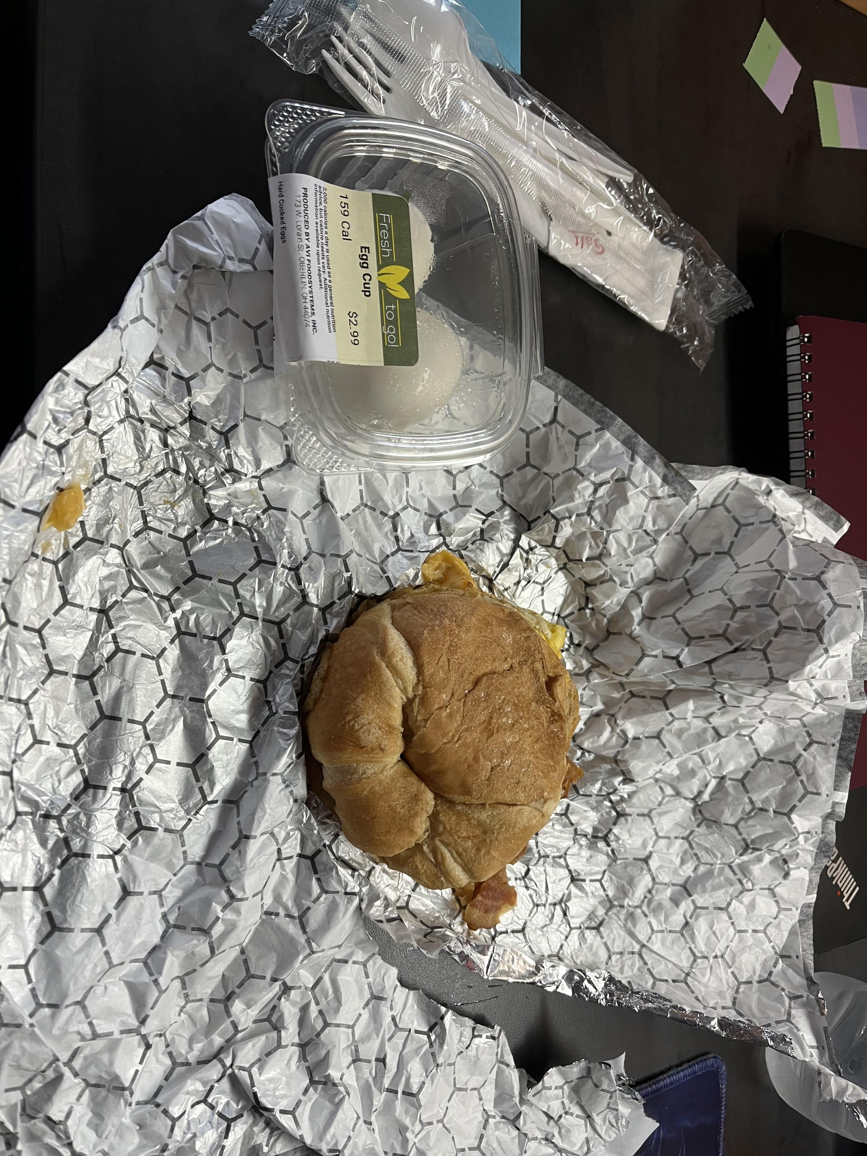 A small breakfast sandwich in unwrapped paper with a container of hard boiled eggs from Sky Bar.