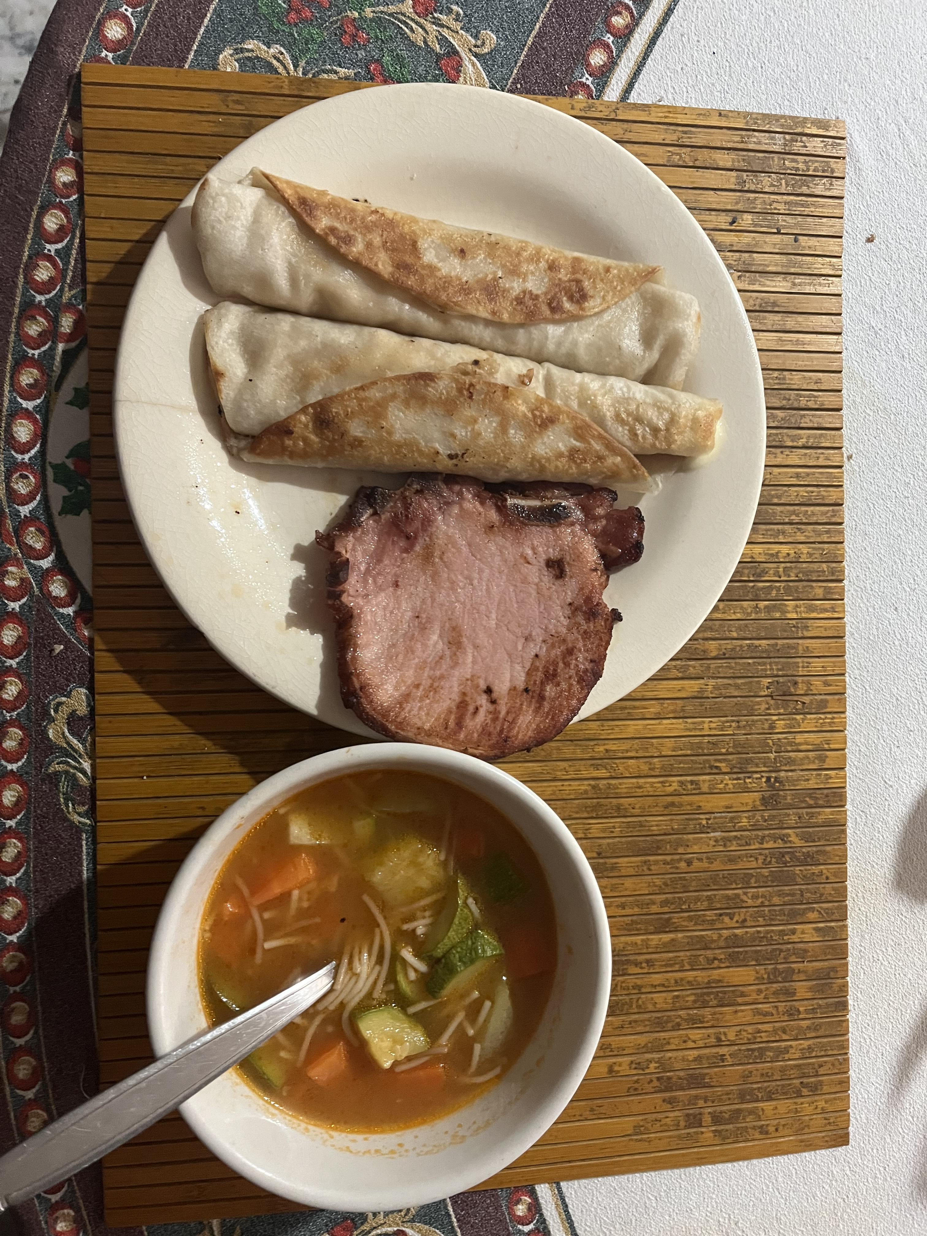 A meal of taquitos, pork, and a vegetable soup.