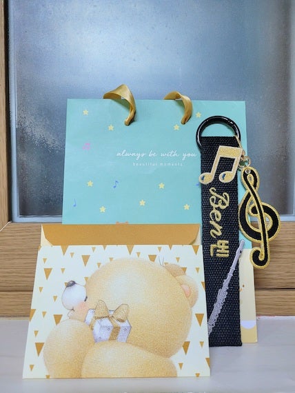A custom-made embroidered key-chain with two eighth notes, a treble clef, my name in English and Korean, and a silver flute on it alongside a letter with a cute bear design.