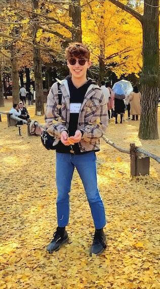 Me standing and smiling with outstretched hands surrounded by a blanket of yellow leaves at Namiseom.