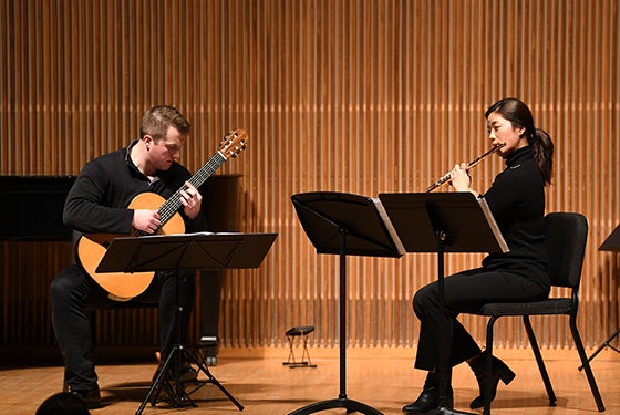 two students performing on guitar and flute