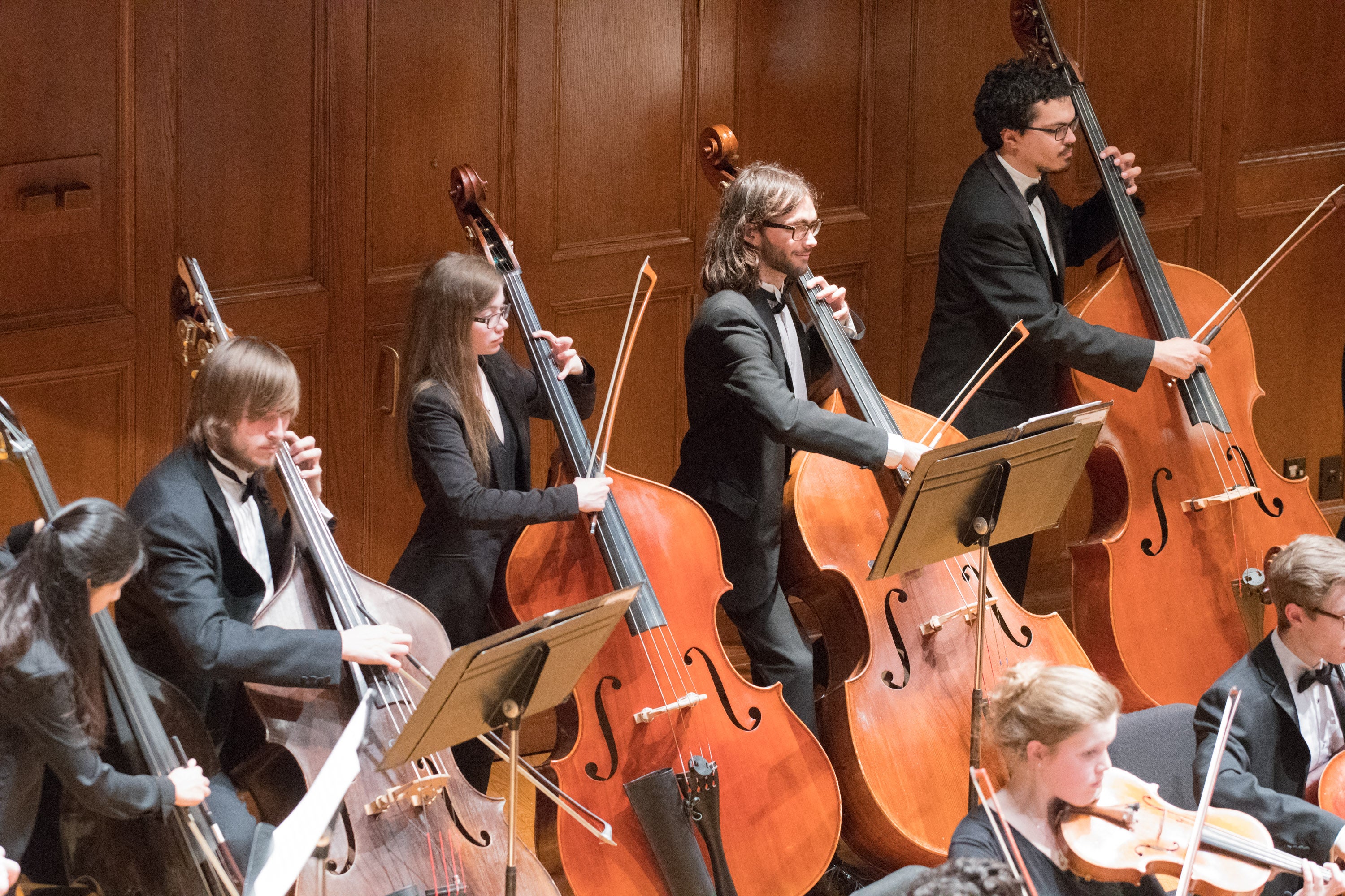Five double bassists performing in an orchestra on the Finney Chapel stage.