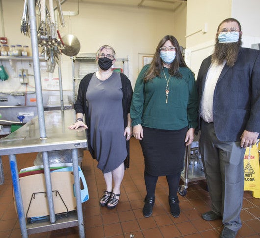 Three people standing should-to-shoulder in commercial kitchen