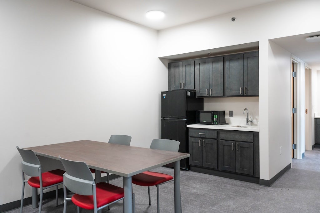 Photo of kitchenette in suite showing dining table with four chairs, fridge, microwave, kitchen storage, and sink