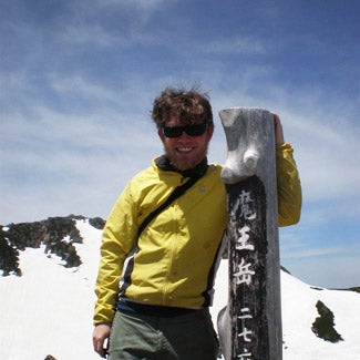 With a snowy mountaintop in the background, Andy stands at a wood post marked with Japanese writing