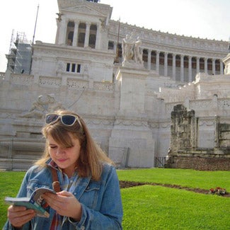 Claire reads a book in front of a classical structure with columns and statues