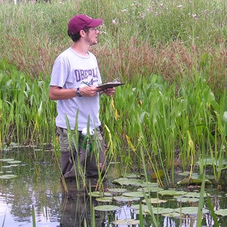 Knee deep in water, Jake studies the surrounding plants and makes notes on a clipboard