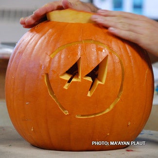 A pair of hands places the top on a jack-o-lantern