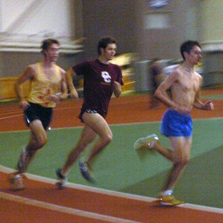Three runners round the bend on an indoor track