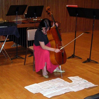 A cellist practices with the score laid out on the floor.