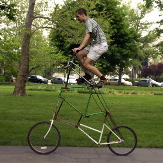 Sam rides atop an improbably tall bicycle.