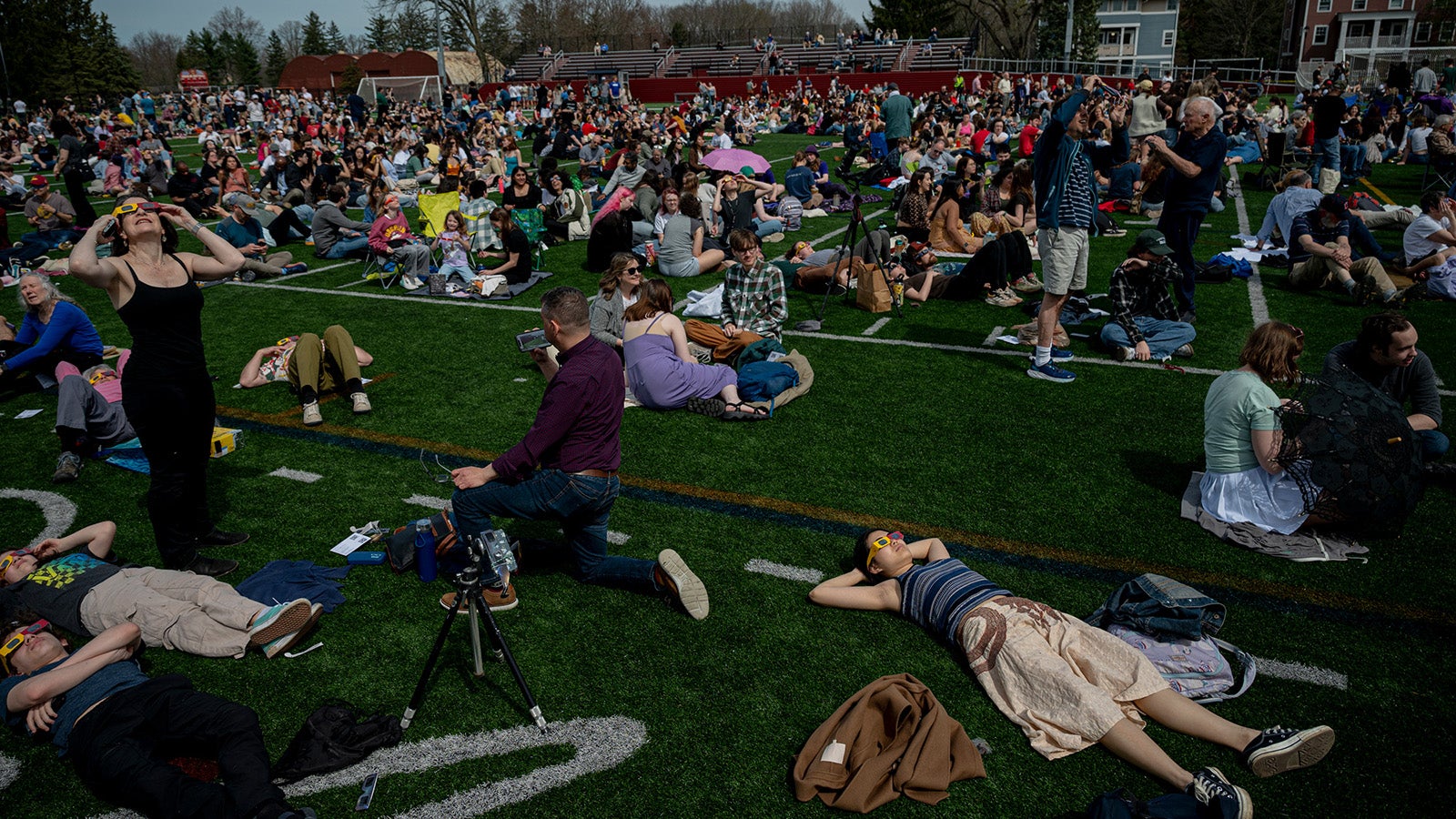 People laying out in the grass wearing eclipse glasses, under the dim light of a solar eclipse.