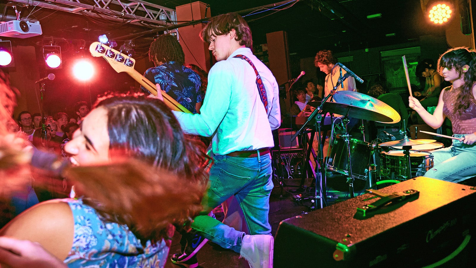 A student rock band performs in a club while people dance.