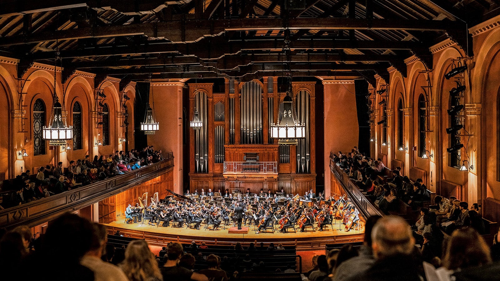 A view from the rear balcony of an orchestra on stage playing to a full house.