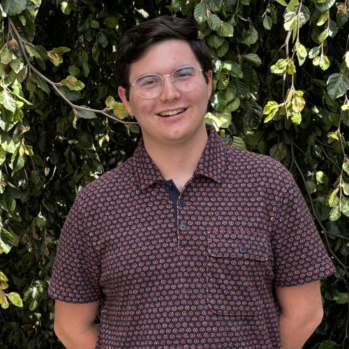 A male Oberlin student in a red shirt standing in front of a tree.