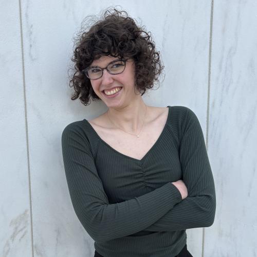An Oberlin student in a gray shirt standing in front of a white wall.