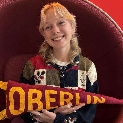 An Oberlin student with blonde hair sitting in a red chair.