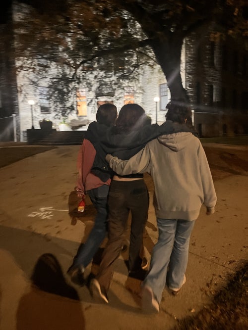 Three girls walking away, arms over each other's shoulders