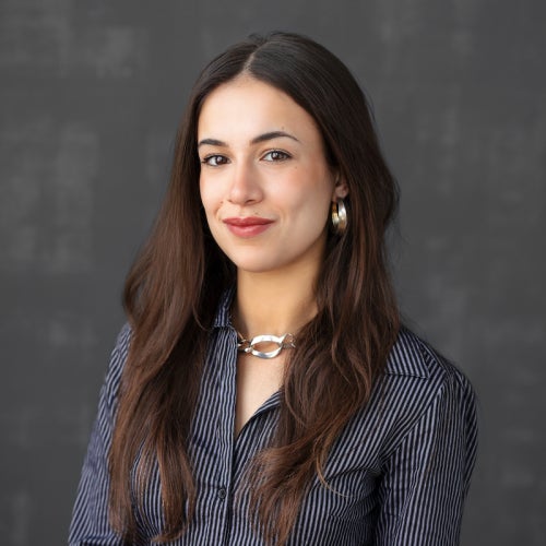 a person with long dark brown hair wearing a dark blue shirt and jewelry
