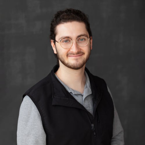 a photo of someone wearing glasses, a black vest and gray shirt