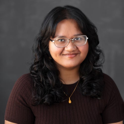 a person with short dark hair and glasses wearing a dark brown shirt
