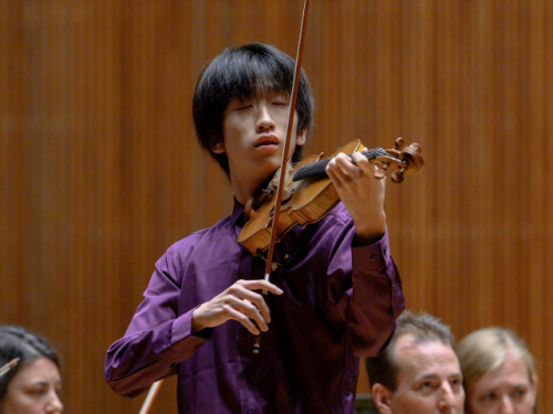 young man in purple shirt playing violin onstage