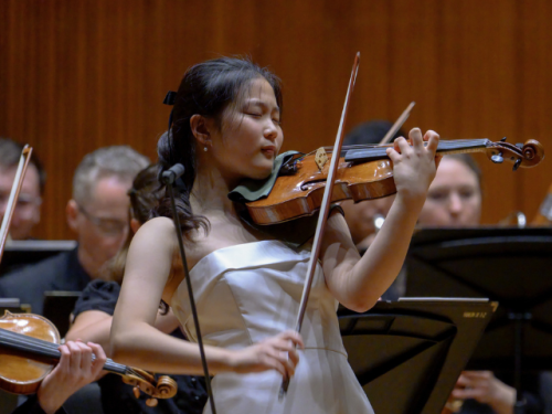 young woman in white dress playing violin onstage
