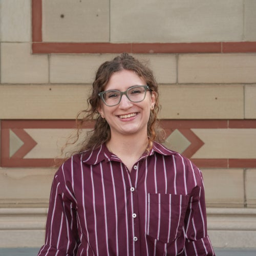 A headshot of a student in a red shirt with curly hair.